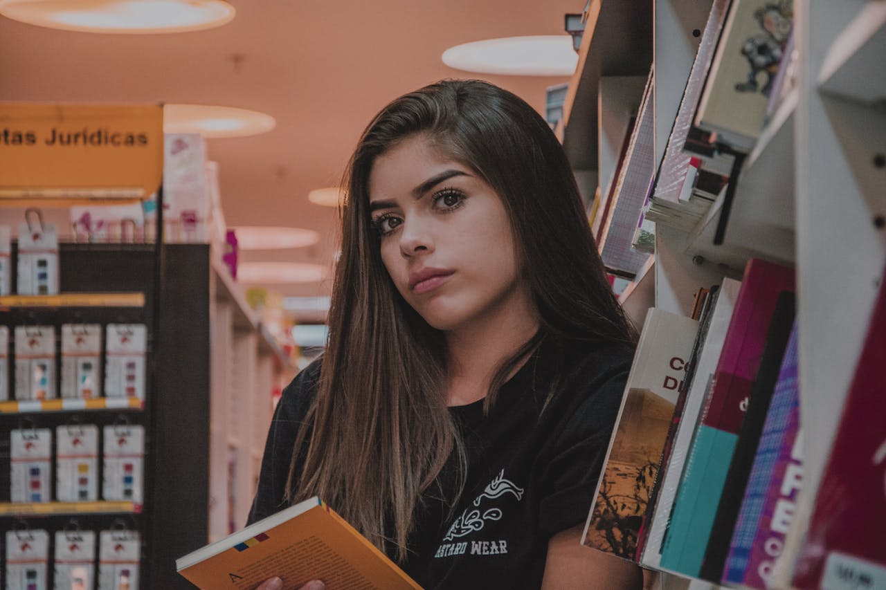 A young woman with long hair reading a book in a cozy bookstore aisle.